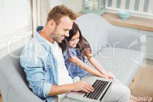 Smiling father and daughter using laptop while sitting on sofa