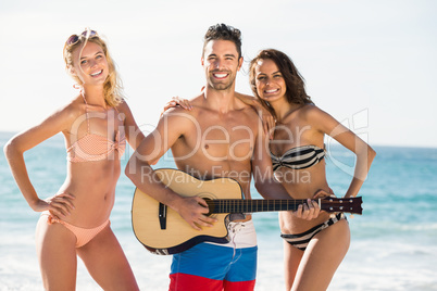 Happy friends posing and playing guitar on the beach