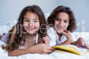 Portrait of brother and sister reading book together on bed