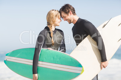 Happy couple standing head to head with surfboard