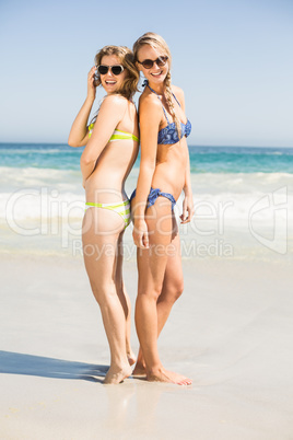 Two happy women in bikini and sunglasses standing back to back