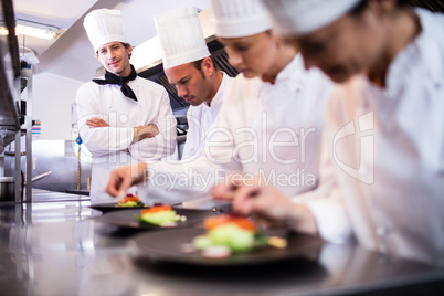 Head chef overlooking other chef preparing dish