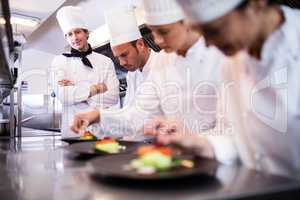 Head chef overlooking other chef preparing dish
