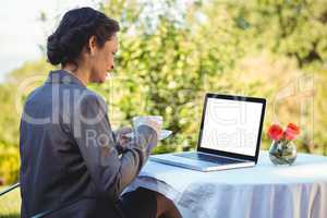Pretty businesswoman having coffee and using laptop