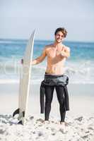 Portrait of man with surfboard showing his thumb up on the beach