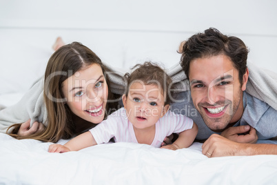 Portrait of happy couple with baby lying on bed