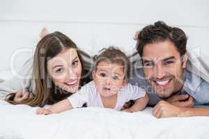 Portrait of happy couple with baby lying on bed