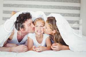 Parents kissing daughter covered with duvet