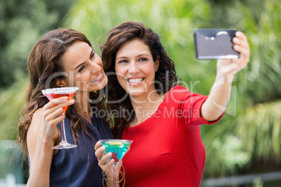 Smiling friends taking self portrait while holding drinks