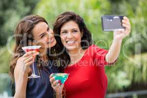 Smiling friends taking self portrait while holding drinks