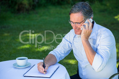 Casual businessman taking notes and having a phone call