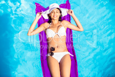 Woman in white bikini lying on air bed in pool