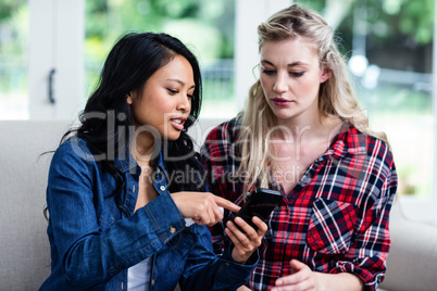 Young woman showing mobile phone to female friend