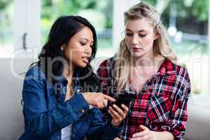 Young woman showing mobile phone to female friend