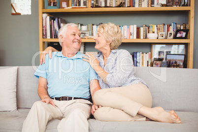 Happy senior couple sitting on sofa against bookshelf