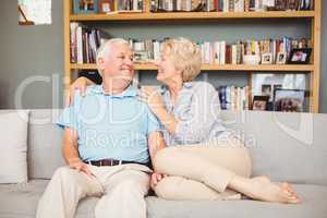 Happy senior couple sitting on sofa against bookshelf
