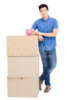 Young man standing near cardboard boxes with piggy bank