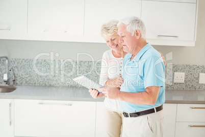 Senior couple laughing while using tablet in kitchen