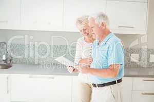 Senior couple laughing while using tablet in kitchen