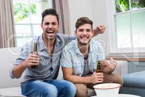 Young male friends enjoying beer while sitting on sofa