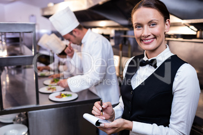 Smiling waitress with note pad in commercial kitchen