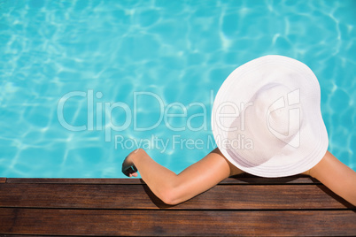 Woman wearing hat leaning on wooden deck by poolside