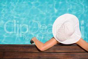 Woman wearing hat leaning on wooden deck by poolside