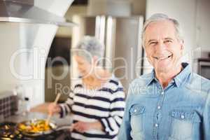Portrait of senior man with woman cooking in background