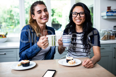 Young female friends holding coffee mug during breakfast
