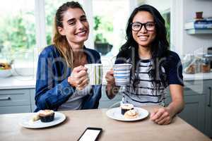 Young female friends holding coffee mug during breakfast