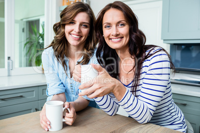 Portrait of smiling female friends holding coffee mugs while sit