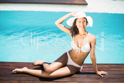 Portrait of happy woman in hat sitting on wooden decker by pool