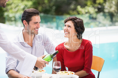 Waiter serving red wine to couple