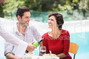 Waiter serving red wine to couple