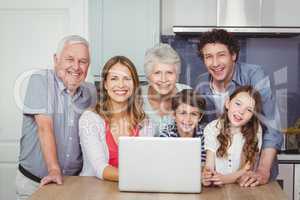 Portrait of smiling family with laptop in kitchen