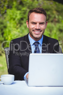 Smiling businessman using laptop and having a coffee