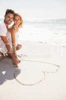 Couple drawing heart on sand