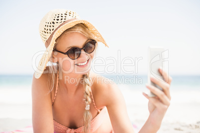 Pretty woman in bikini and sunglasses taking a selfie on the bea