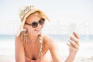 Pretty woman in bikini and sunglasses taking a selfie on the bea