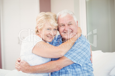 Senior couple looking away while embracing in bedroom