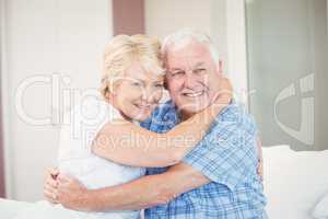 Senior couple looking away while embracing in bedroom