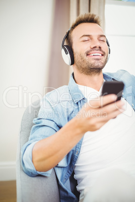 Smiling man listening to music while holding mobile phone