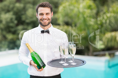 Smiling waiter holding champagne flutes and bottle