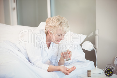 Woman taking medicine while resting on bed