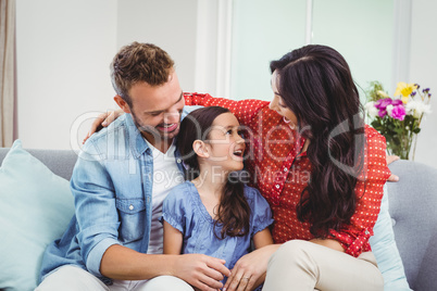 Parents smiling while sitting with daughter on sofa