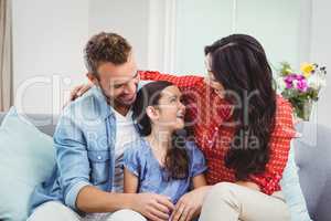 Parents smiling while sitting with daughter on sofa