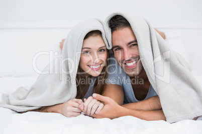 Portrait of happy couple lying under blanket