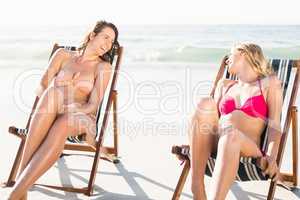 Two women talking while relaxing on armchair on the beach