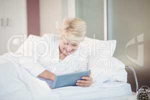 Senior woman using digital tablet while resting on bed