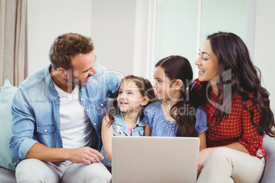 Family smiling and using laptop on sofa